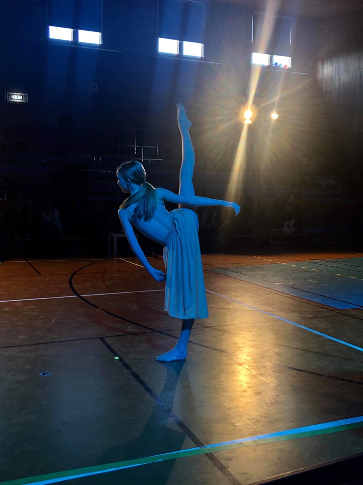 En tjej i klänning står på ett ben med andra benen sträckt i luften