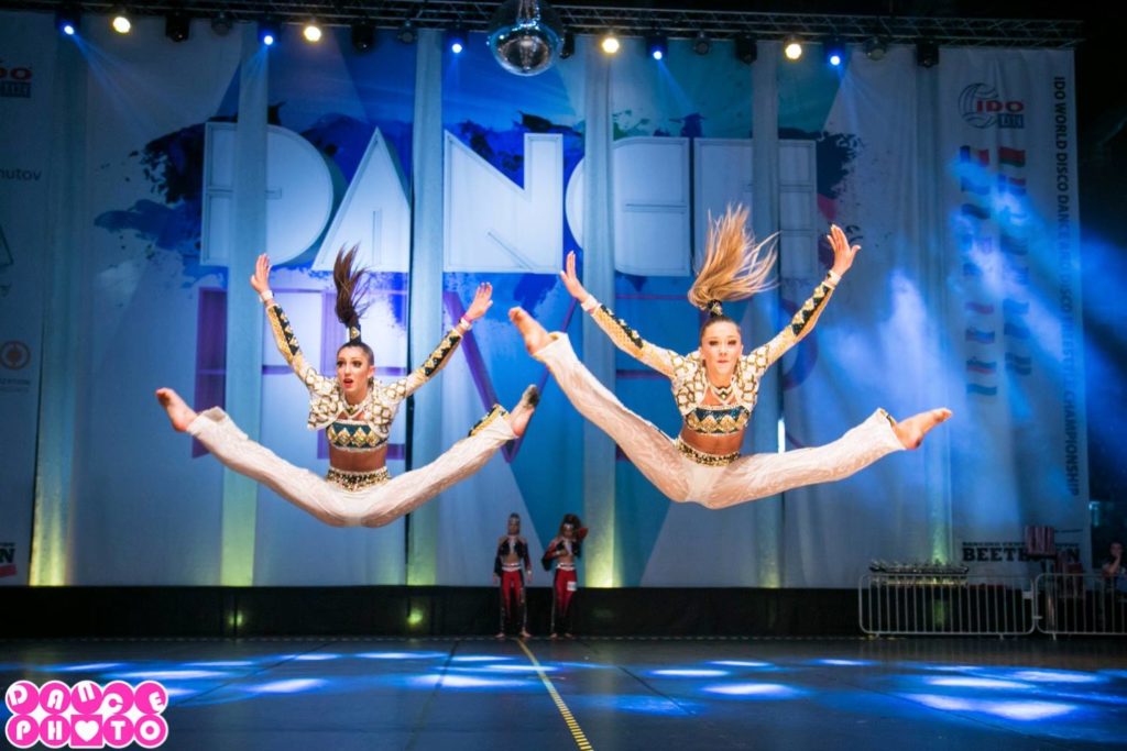 Två tjejer i vita kläder hoppar i split