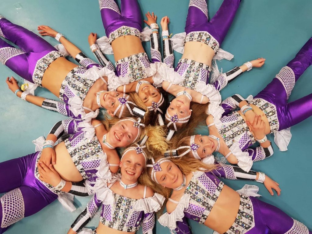 Tjejer i vita och lila kläder ligger i en ring